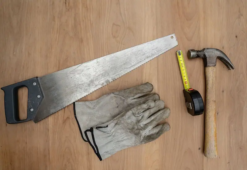 Sag, hammer, målebånd og arbeidshansker på en trebenk